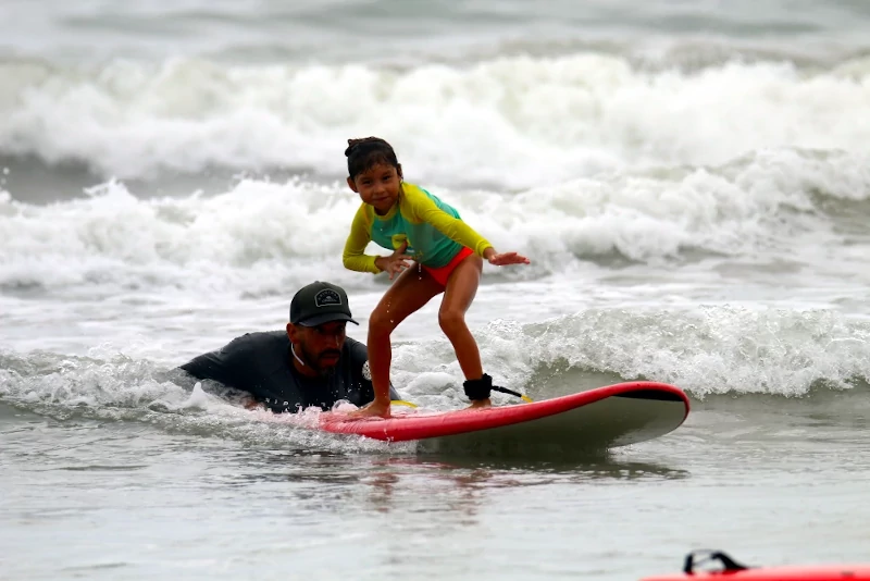 Girl is being pushed by instrutor while riding a surfboard