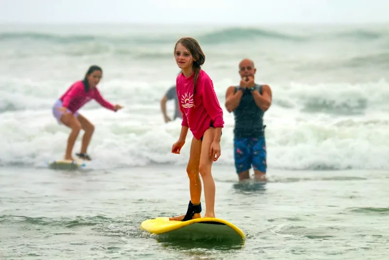 Two girls surfing while their instructors are constantly watching